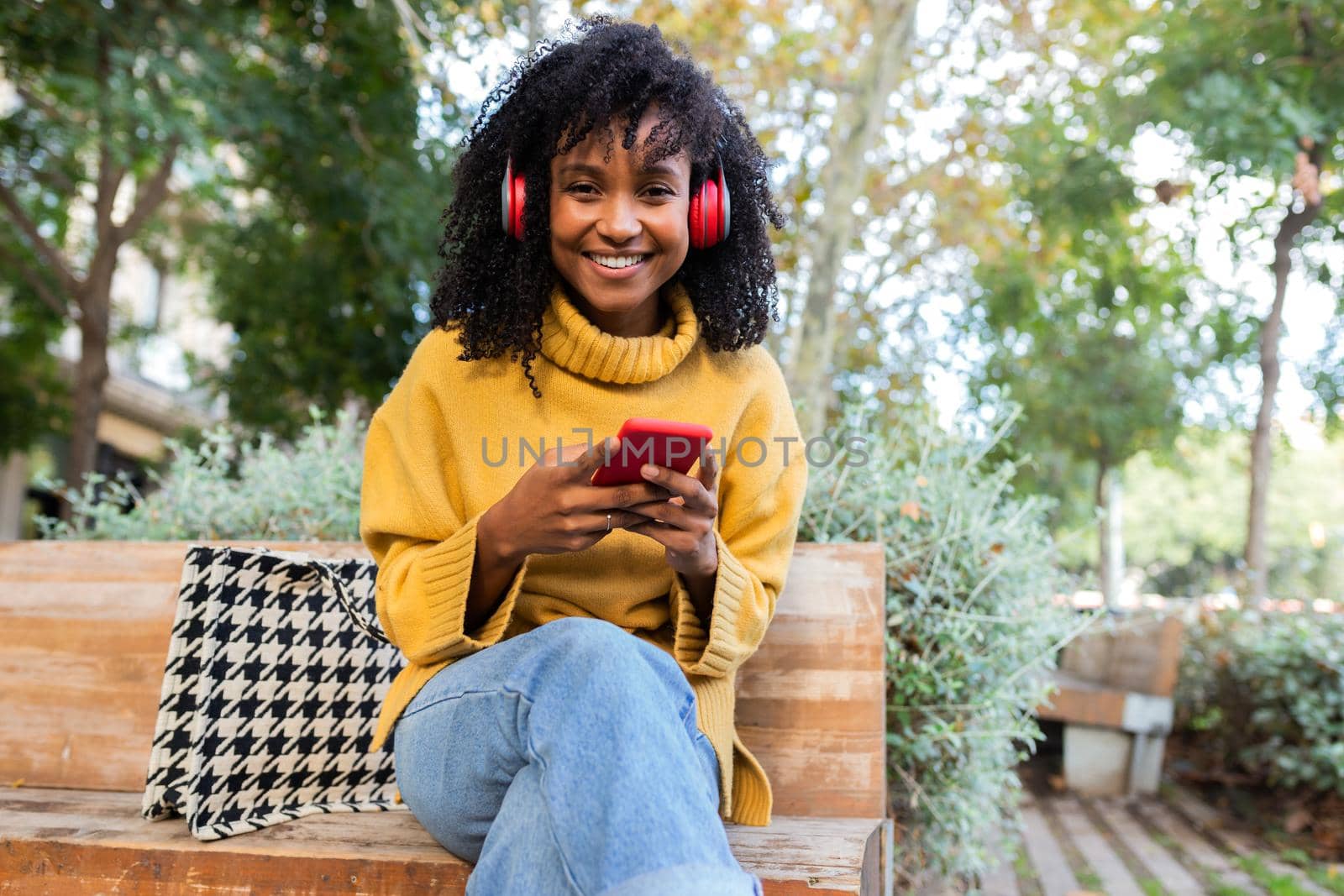 African American woman with headphones uses cellphone on park bench. Copy space. by Hoverstock