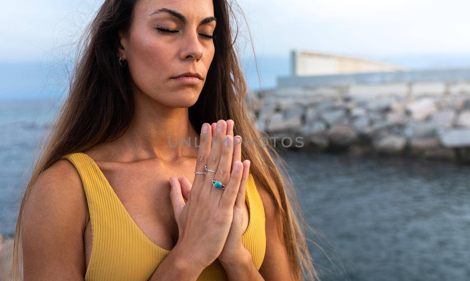 Portrait of young caucasian woman with hands in namaste mudra praying and meditating near the sea. Copy space. Spirituality and mindfulness concept.
