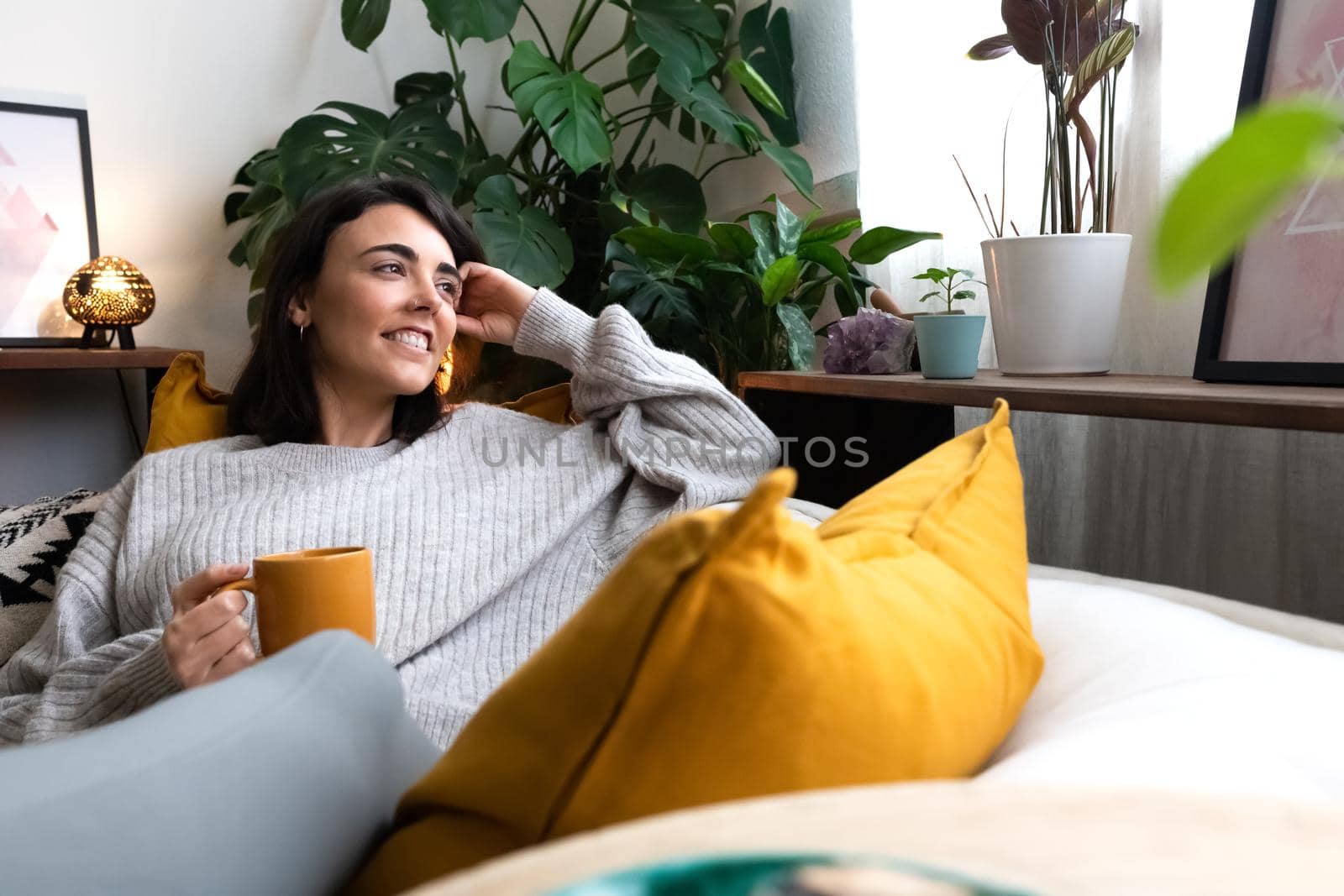 Happy young woman relaxing at home with tea looking out the window. Copy space. by Hoverstock