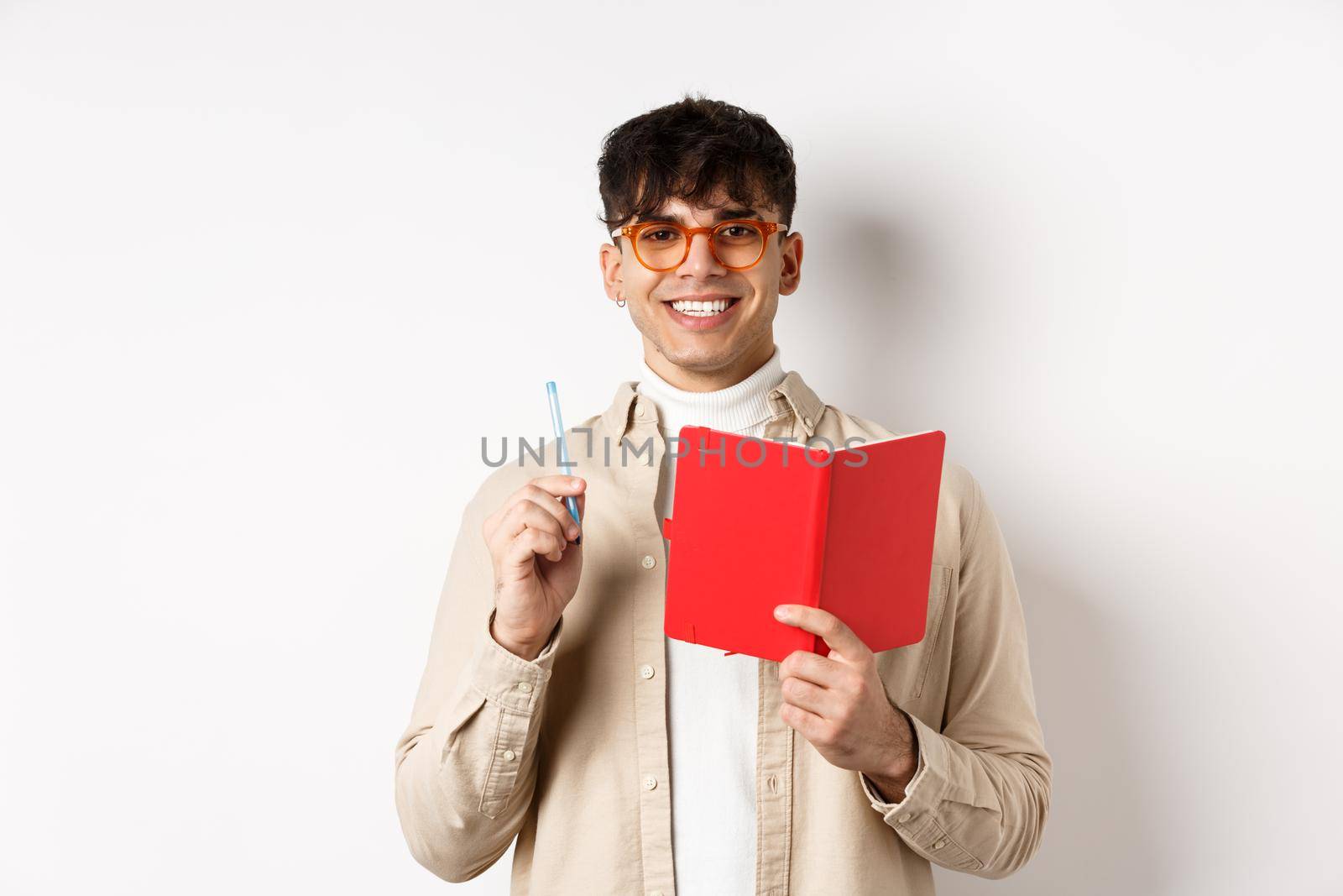 Happy person in glasses writing in journal, holding pen and diary, smiling at camera, plan a schedule, standing with planner on white background.