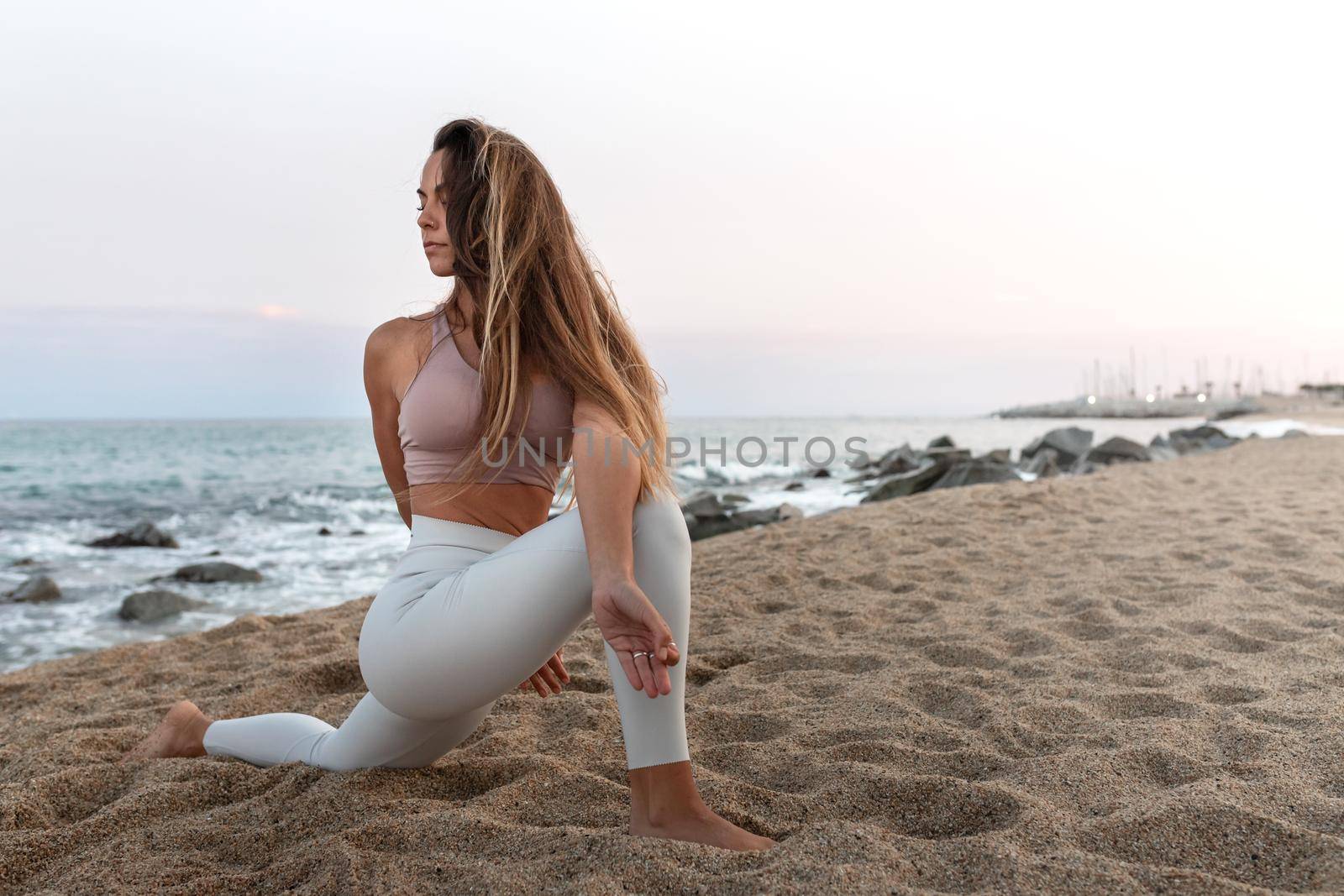 Young woman practicing yoga asana twist on the beach at sunset. Copy space. Spirituality and healthy lifestyle concept.