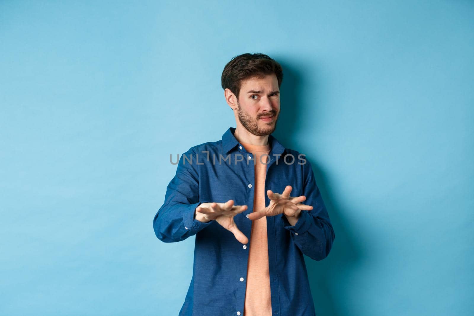 Guy cringe from something awful and nasty, refusing from bad ofer, looking disgusted, standing on blue background. Copy space