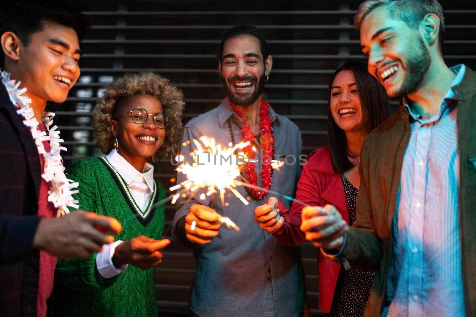 Smiling young multiracial friends having night party with sparklers. Friendship and lifestyle concept.