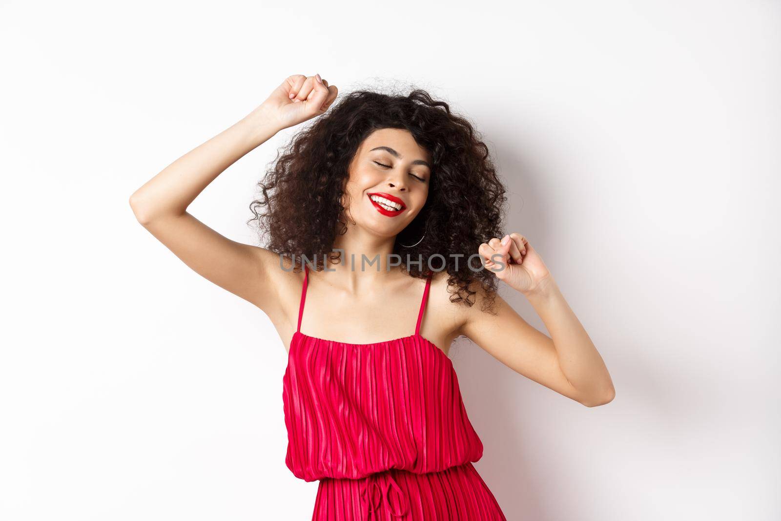 Happy elegant woman in red dress dancing on white studio background.