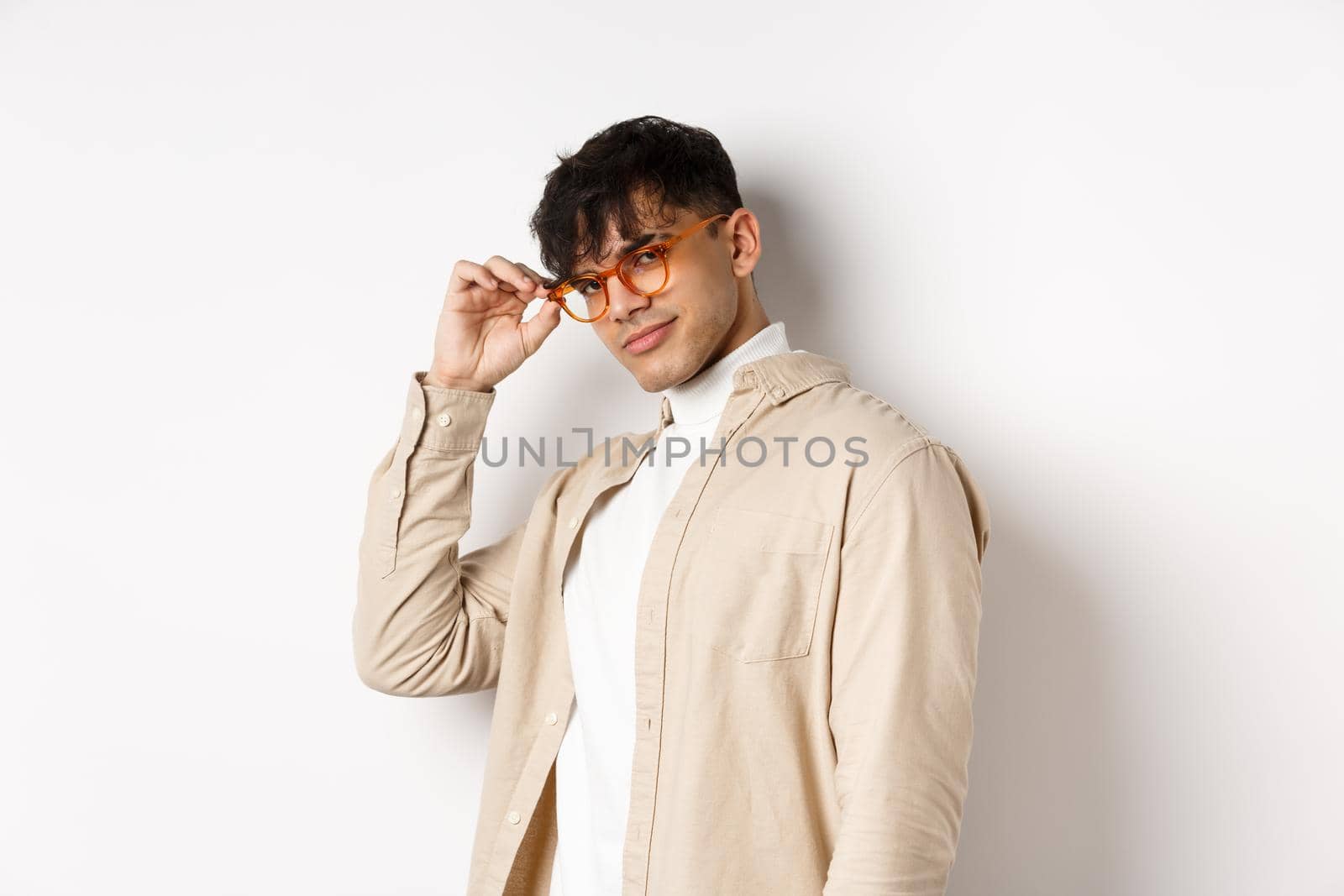 Handsome stylish guy saluting you, touching eyewear and smiling sassy, standing on white background.