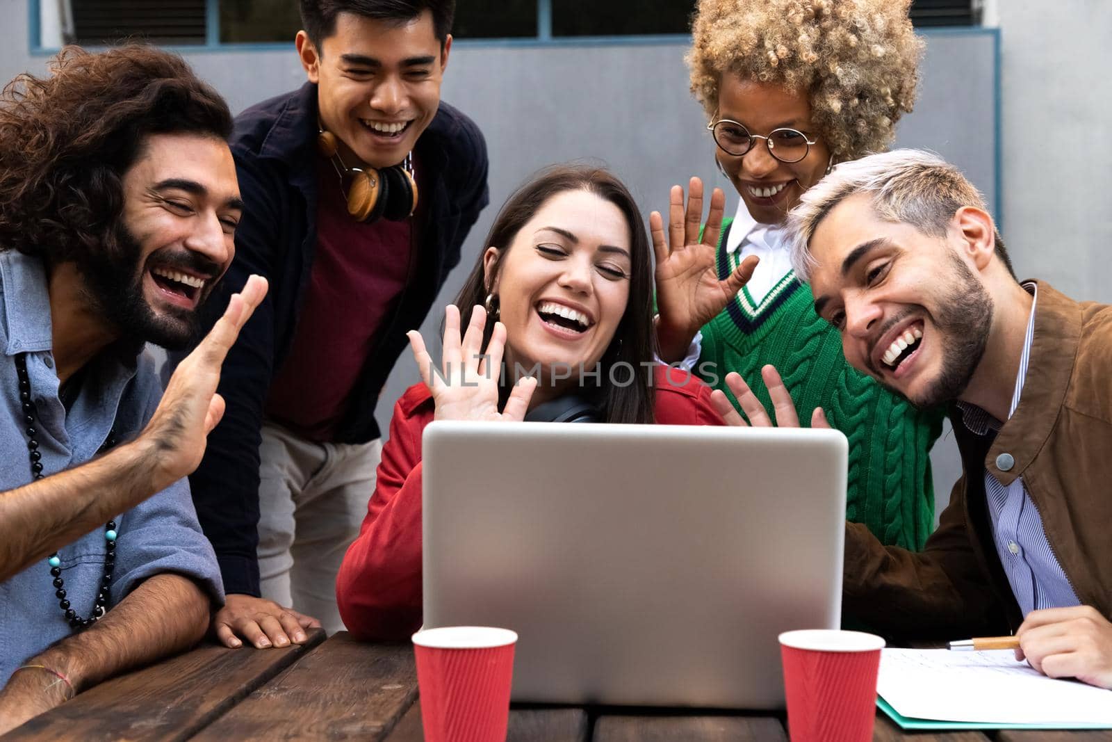 Smiling multiracial group of friends on a video call waving hand saying hello to friend. Friendship and technology concept.