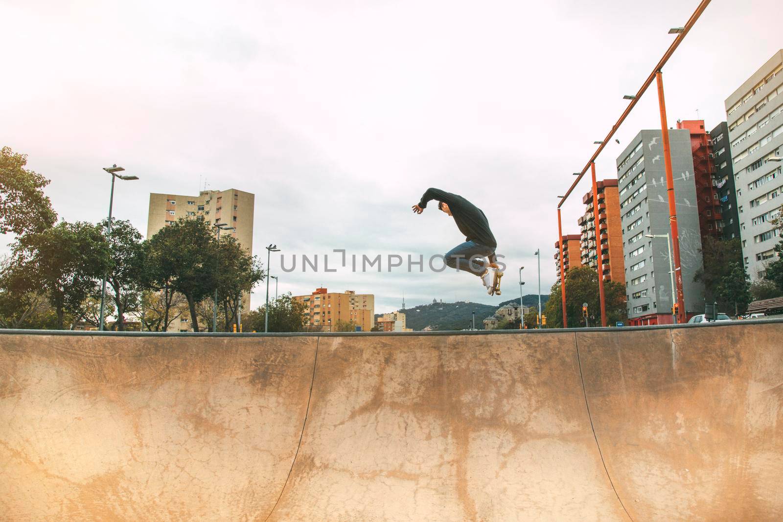 skater jumping high in the air with a snakeboard in a skatepark with white sky and buildings in the background with copyspace