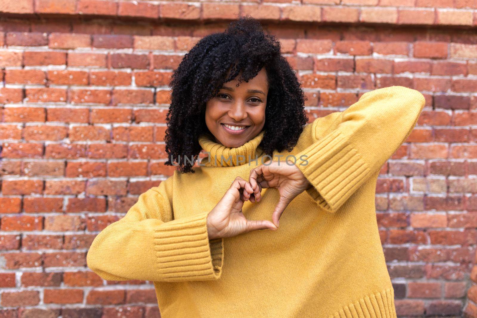 Happy young African American woman making heart shape with hands in front of chest. Love and romance concept.