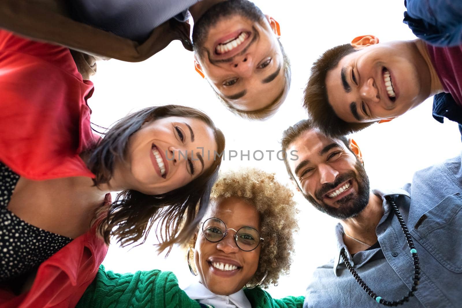 Low angle view smiling multiracial group of friends looking at camera form circle with heads. by Hoverstock