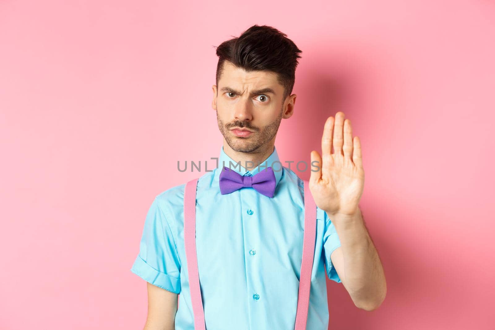 Serious-looking man prohibit something bad, stretch out hand to stop you, forbid action, saying no and looking strict, standing over pink background.