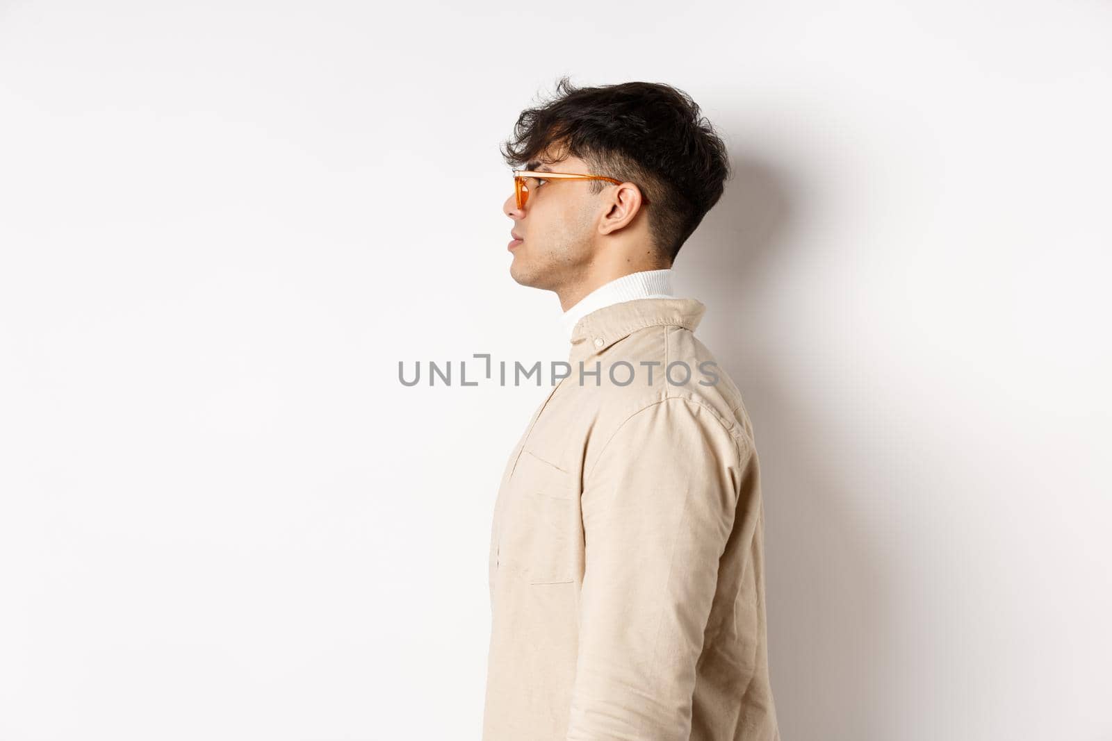 Profile of handsome caucasian man in eyewear, looking at empty space left with serious face, standing on white background.