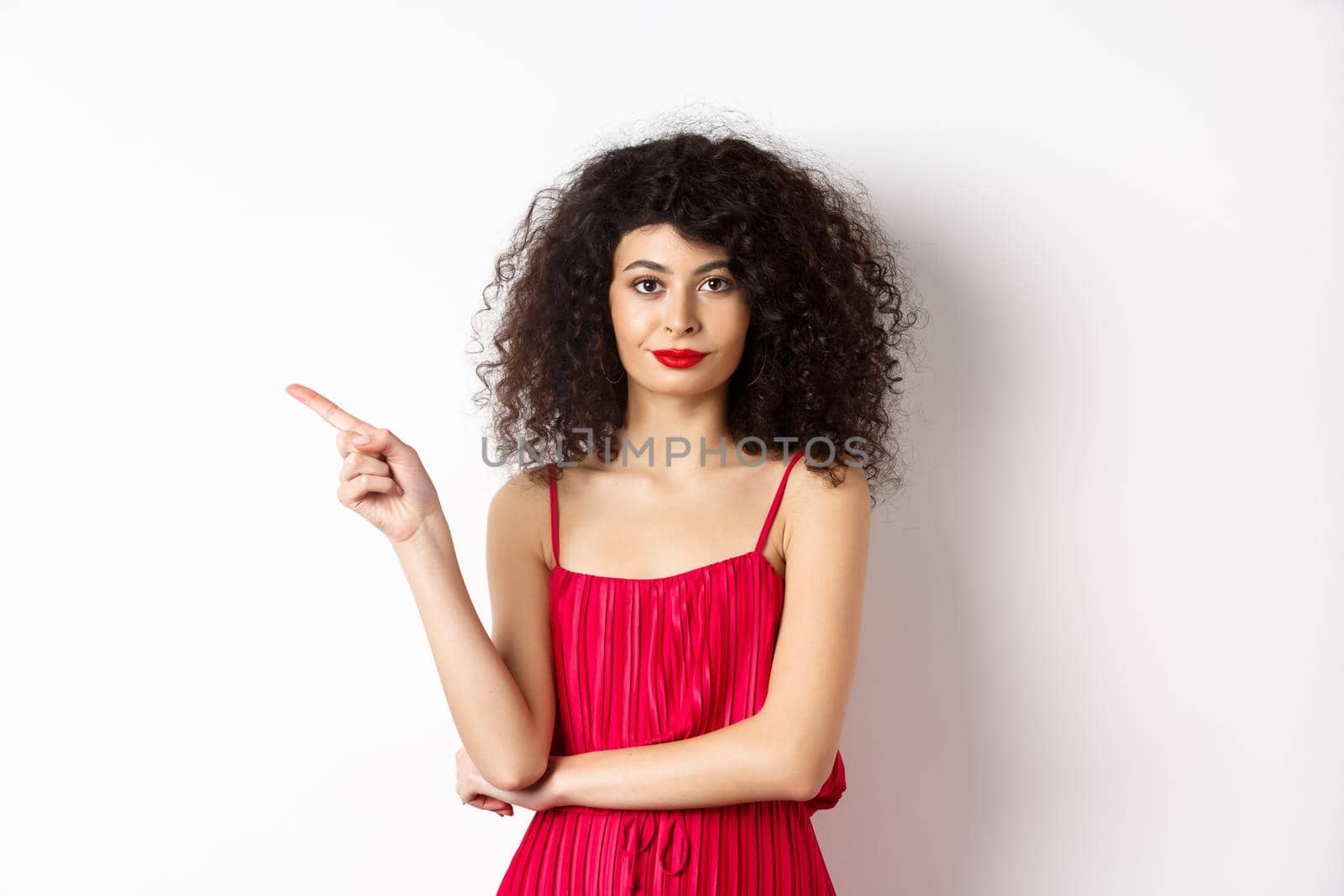 Attractive lady in red dress and makeup pointing finger left, showing logo, standing over white background.