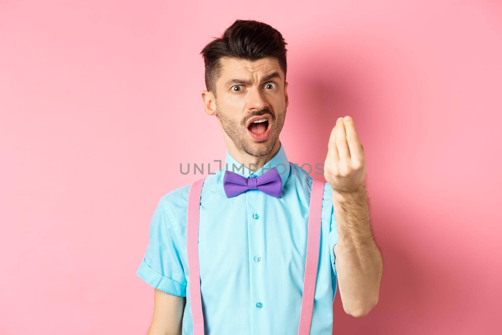 Impulsive young man having an arument, prove someone wrong, showing italian gesture and complaining, standing over pink background by Benzoix