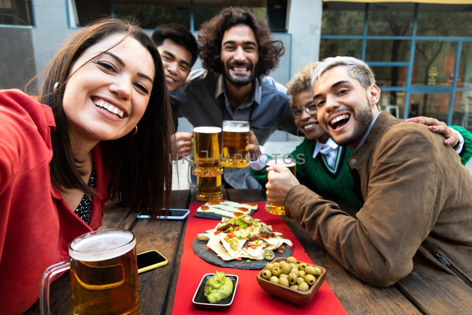 Selfie photo of smiling multiracial friends enjoying some beer in outdoors bar. by Hoverstock