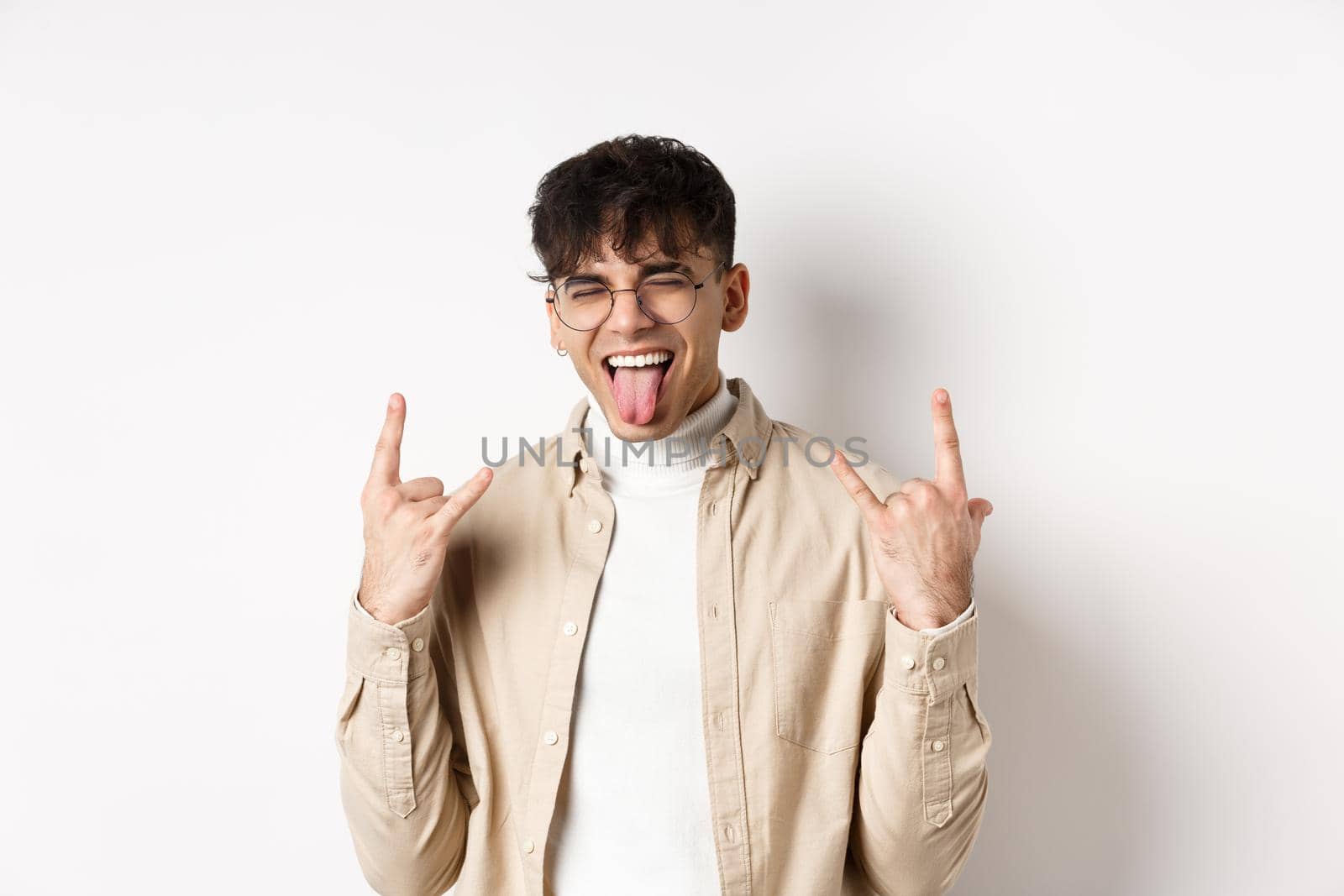 Happy handsome guy showing tongue and rock-on gesture, having fun and feeling upbeat, enjoying something good, standing on white background.