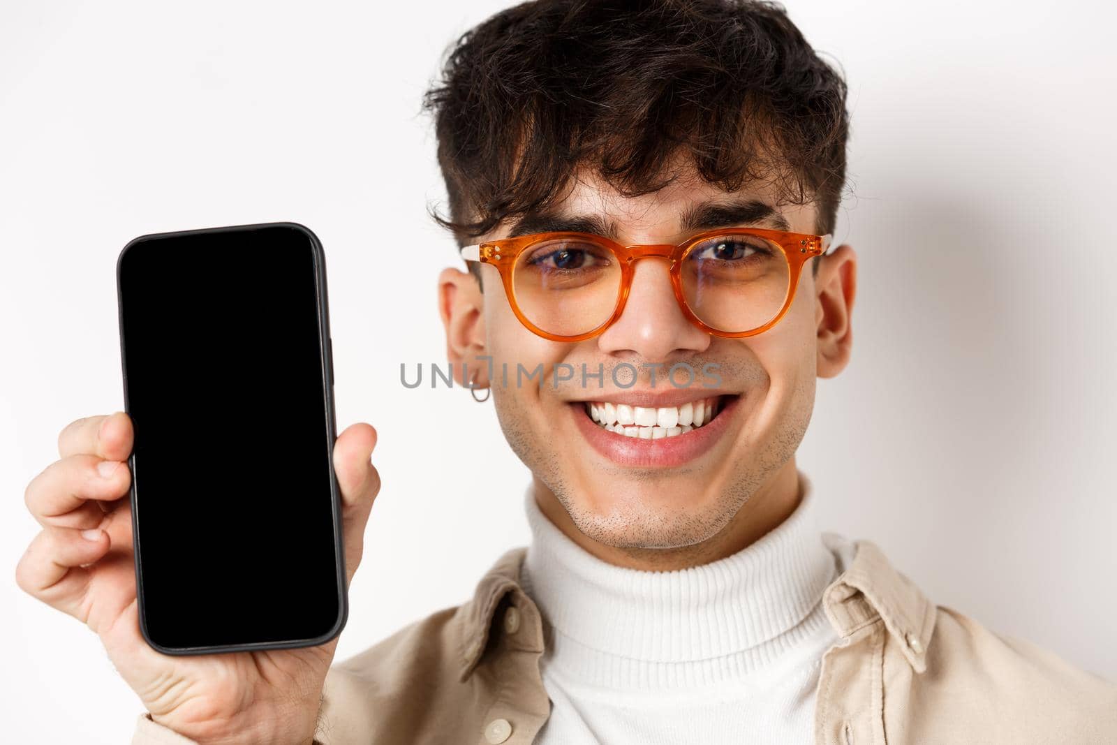 Face of handsome smiling guy in glasses showing empty smartphone scree, white background by Benzoix