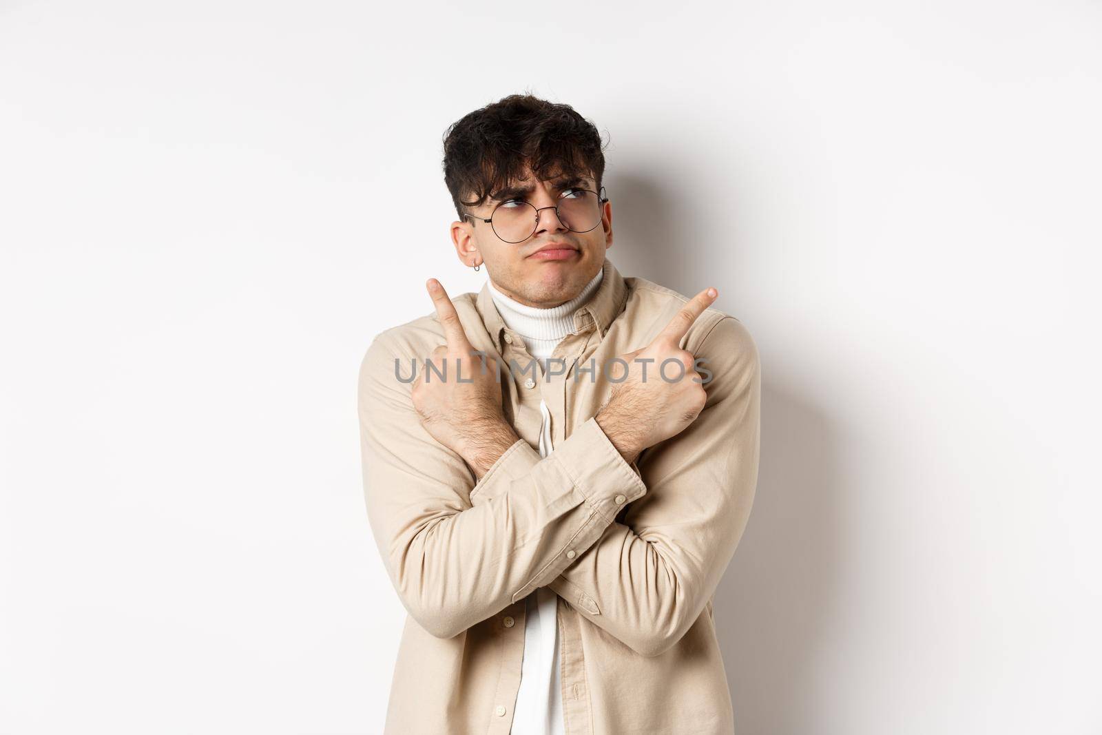 Indecisive funny young man having troubles with making choice, pointing fingers sideways and frowning perplexed, deciding between two variants, standing on white background by Benzoix