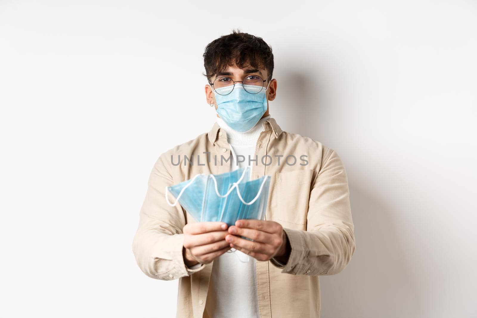 Health, covid and quarantine concept. Image of young guy handing out medical masks for preventive measures, helping during pandemic, standing on white background.