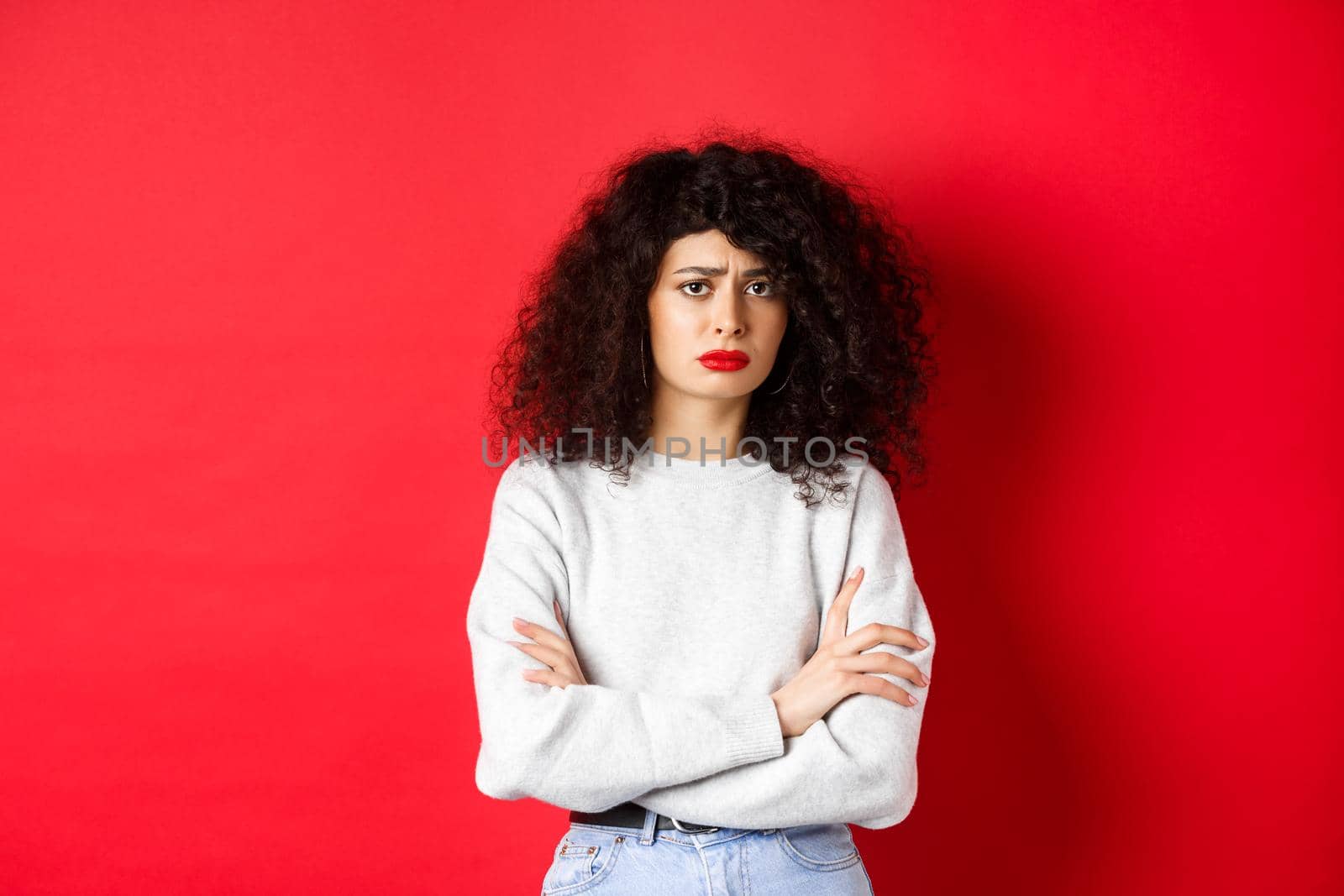 Sad and worried caucasian woman frowning, cross arms on chest and looking concerned, feeling bad, standing on red background by Benzoix