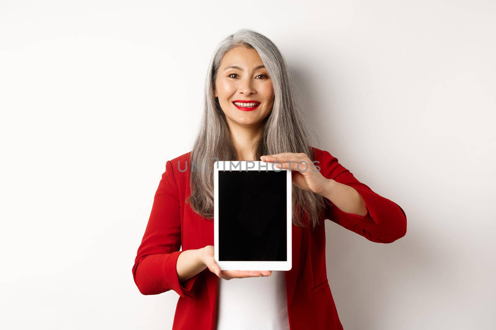 Business. Proud asian female manager showing blank digital tablet screen, smiling and demonstrating promo, standing over white background by Benzoix