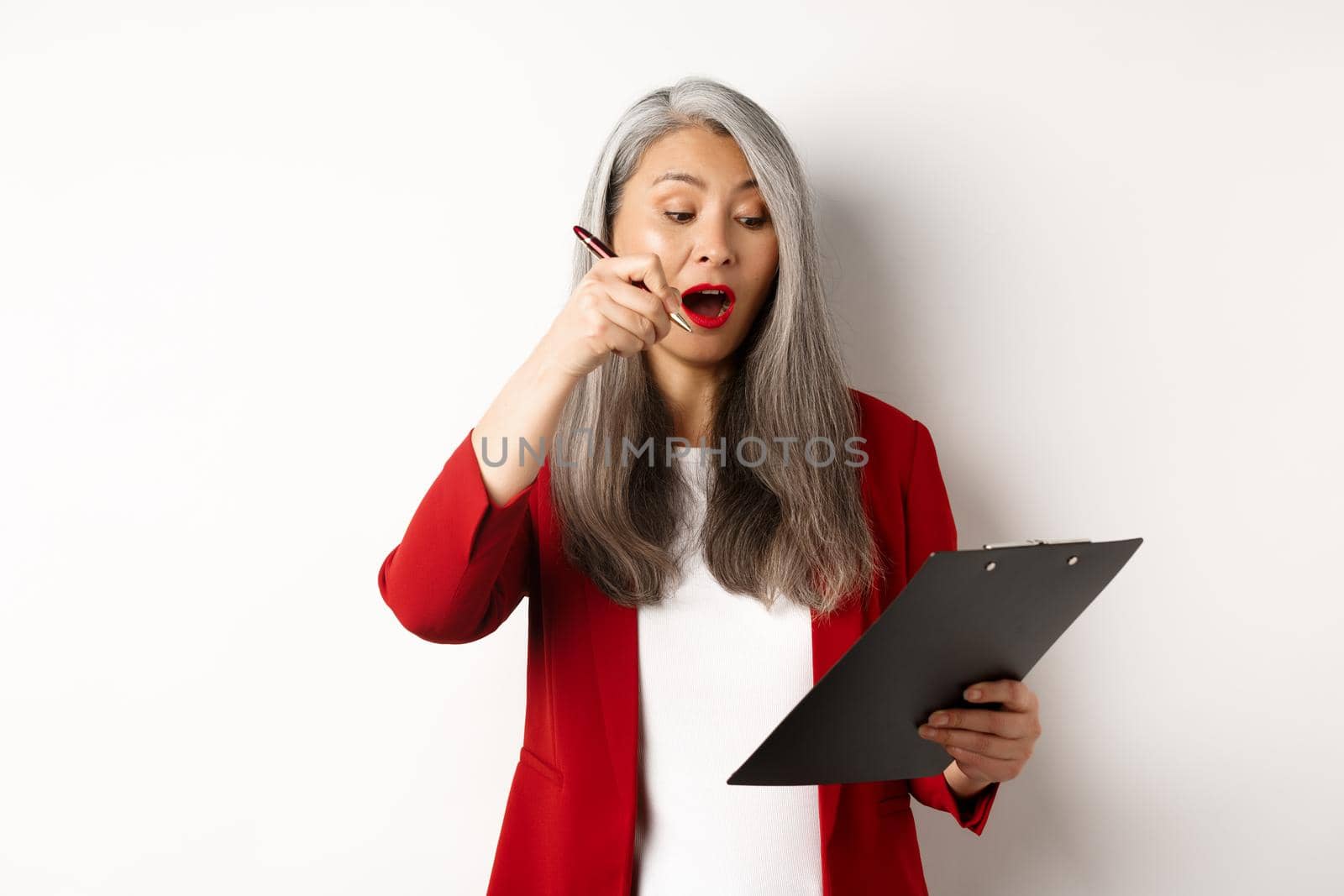 Successful asian female entrepreneur taking notes on clipboard, working on report and looking excited, standing over white background.