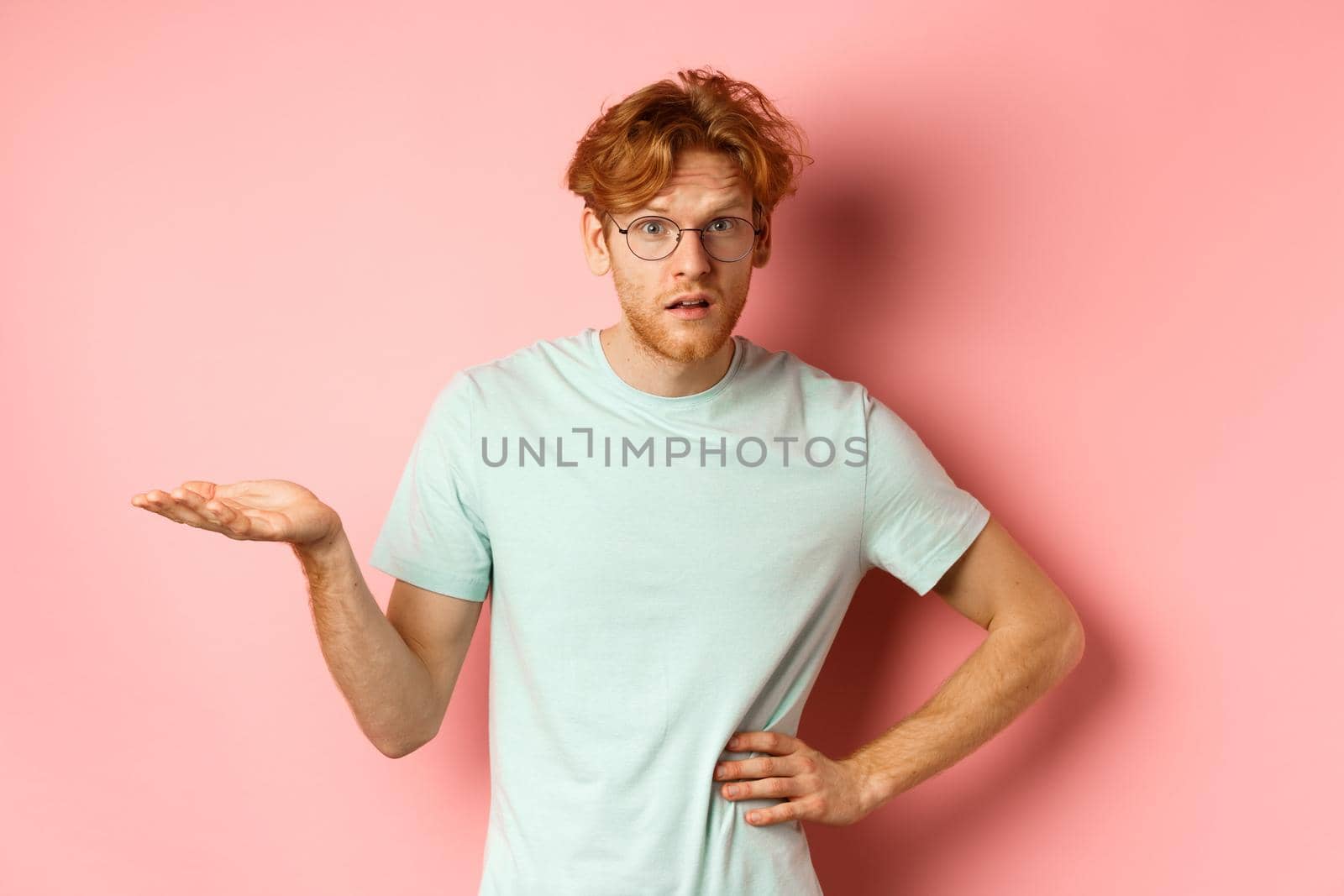 So what. Confused redhead man raising hand and shrugging, looking puzzled, dont understand something, standing over pink background by Benzoix