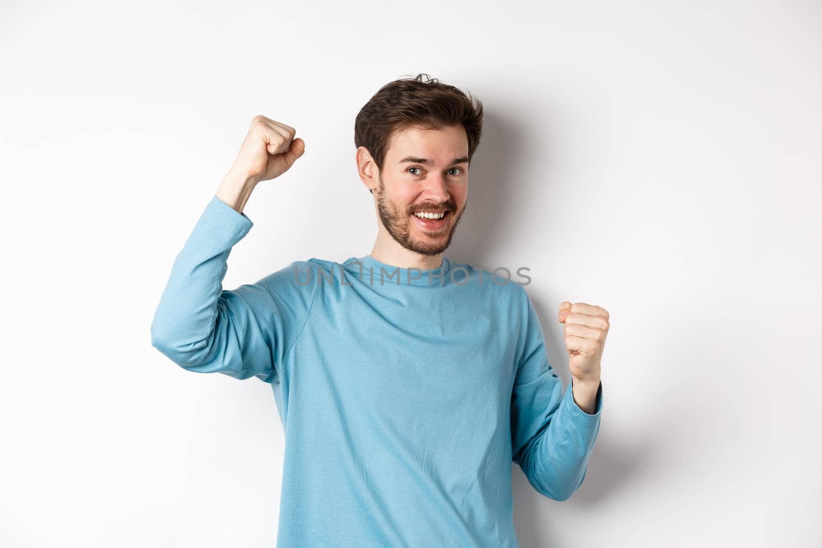 Happy bearded man celebrating victory, raising hands up and triumphing, winning prize and smiling with joy, standing over white background by Benzoix