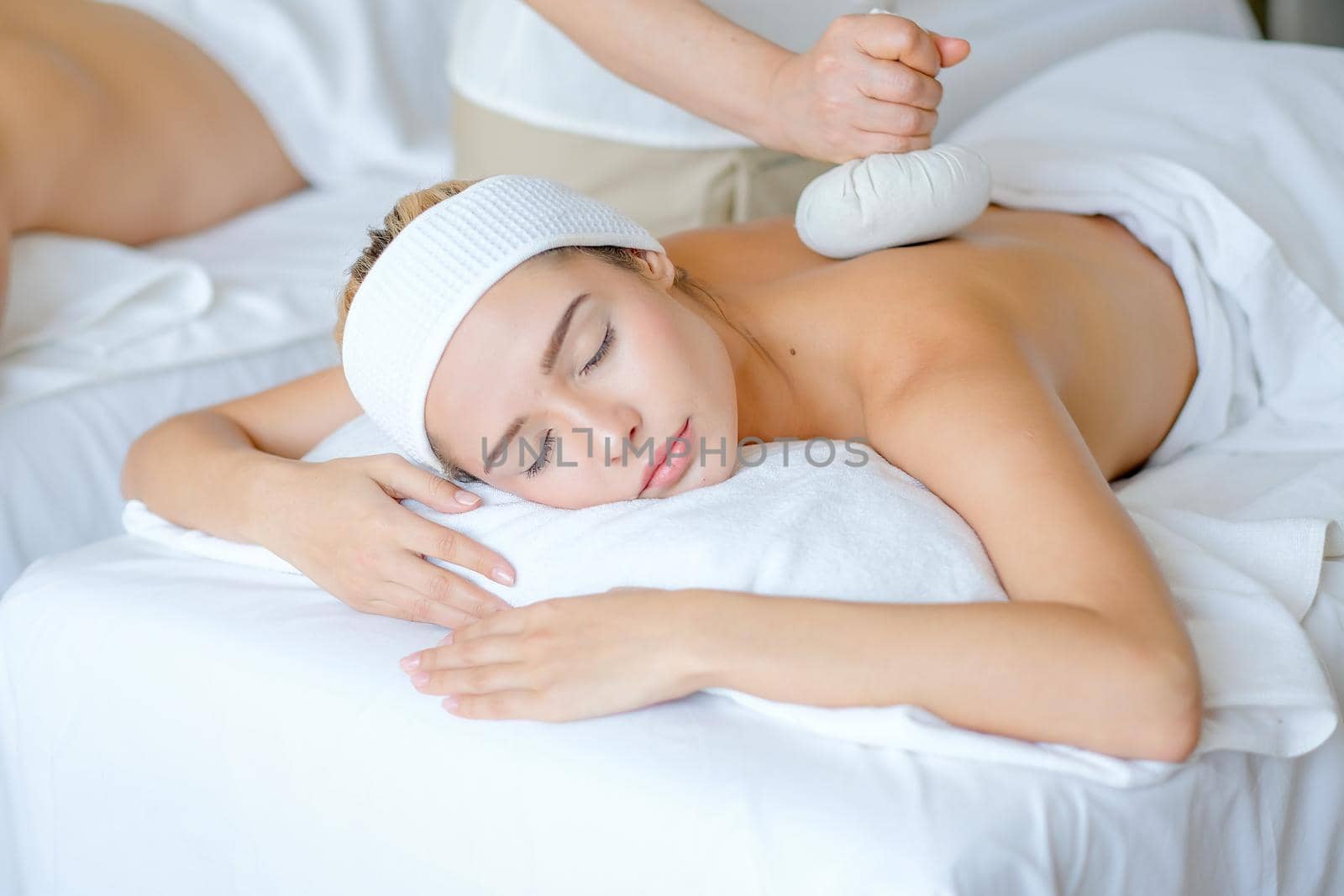 Young beautiful girl enjoy with massage by herbal ball on her back in spa room with day light.