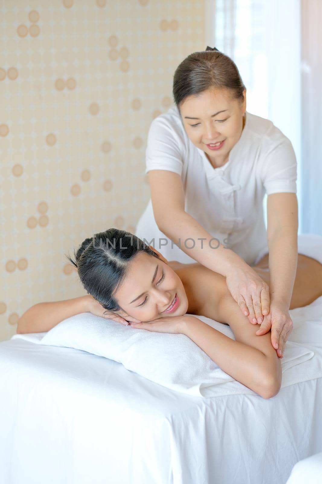 Portrait of Asian beautiful woman lie on bed and get the spa massage in the room with day light.