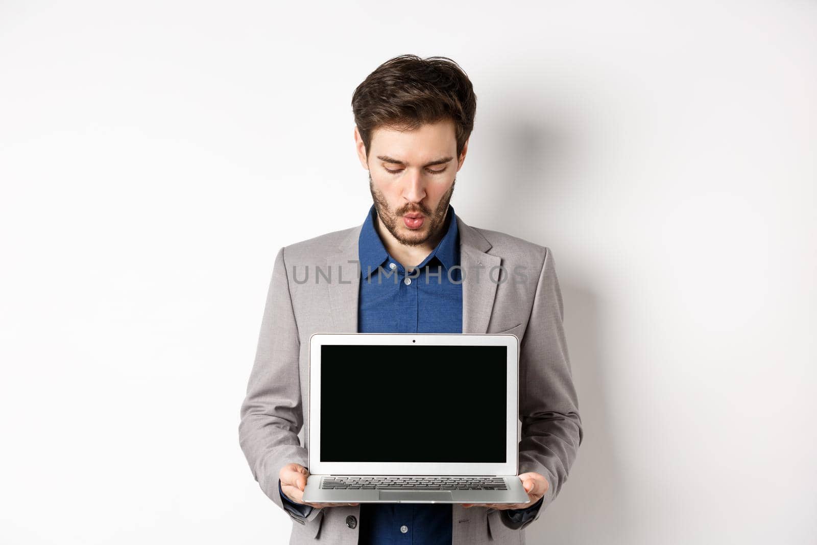 Handsome caucasian businessman in suit showing empty laptop screen, demonstrate promo, standing on white background.