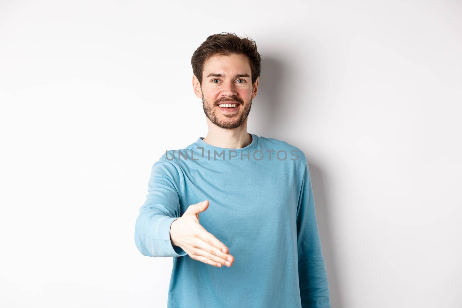 Friendly smiling man stretch out hand, saying hello and give arm for handshake, standing over white background by Benzoix