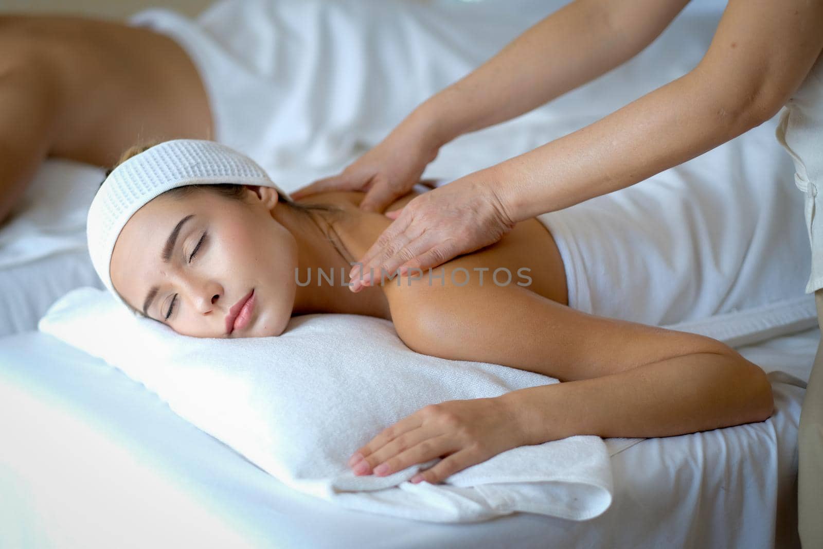 Young beautiful woman enjoy with massage in spa room with day light and the other man lie on bed beside her.