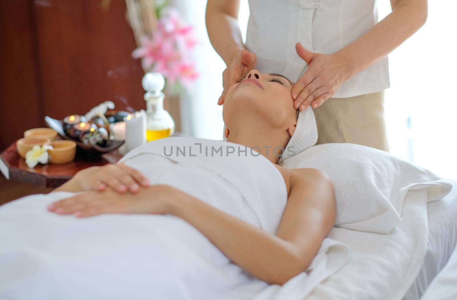 Young beautiful girl enjoying face massage and look up on bed in spa room with day light.