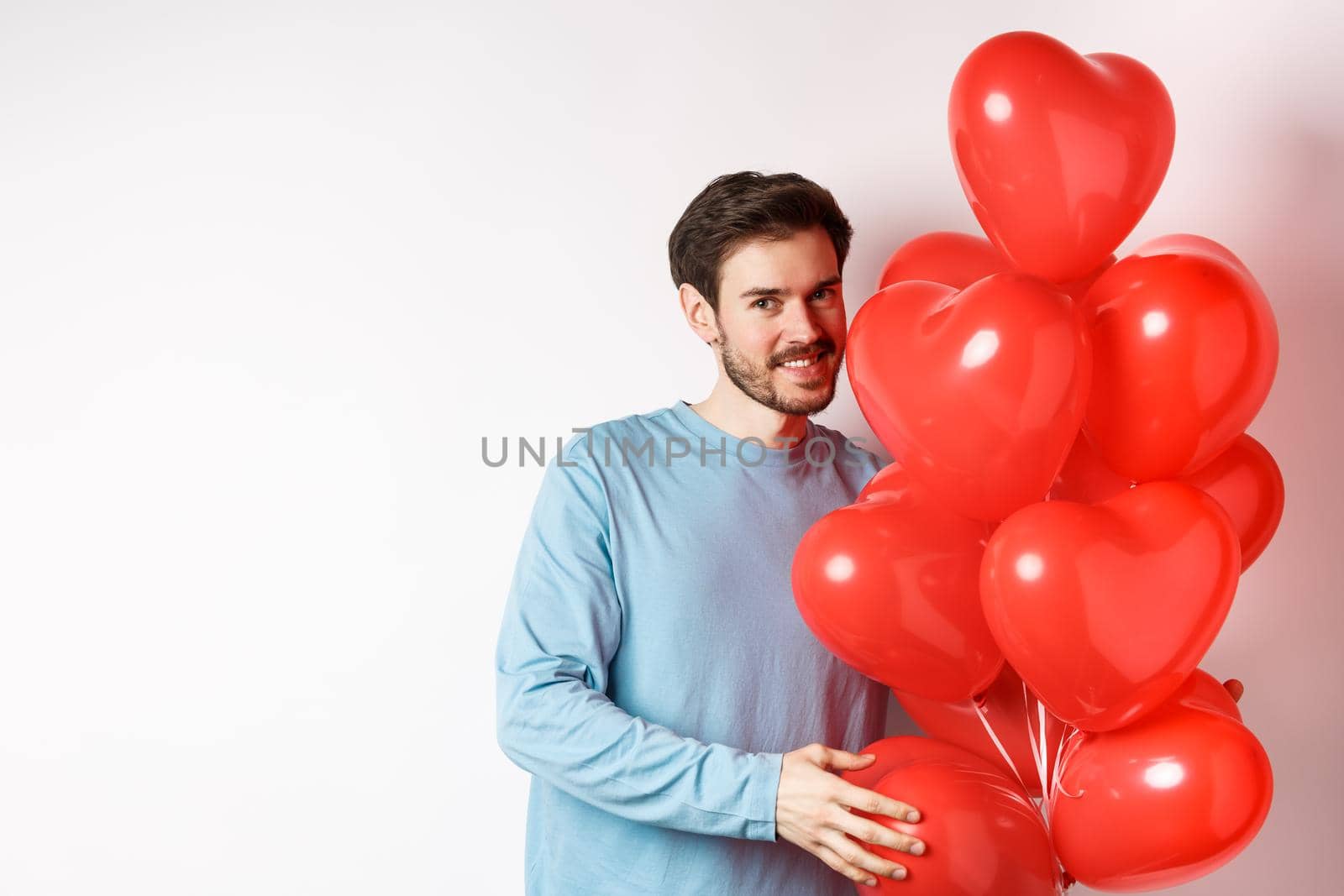 Romantic boyfriend bring red hearts balloons on Valentines day, surprise lover on date, standing over white background by Benzoix