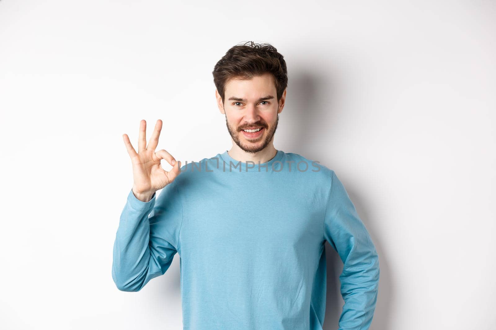 Okay. Handsome smiling man showing ok sign and looking confident, recommend or praise something good, standing over white background by Benzoix