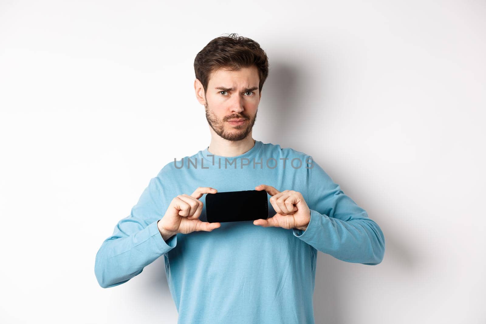 E-commerce and shopping concept. Sad and disappointed guy complaining, showing empty smartphone screen, standing on white background.