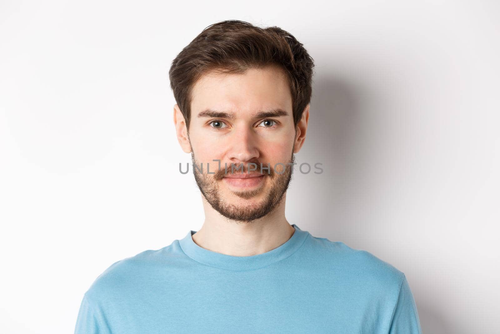 Close up of young handsome man with beard, smiling at camera with confidence, standing over white background.