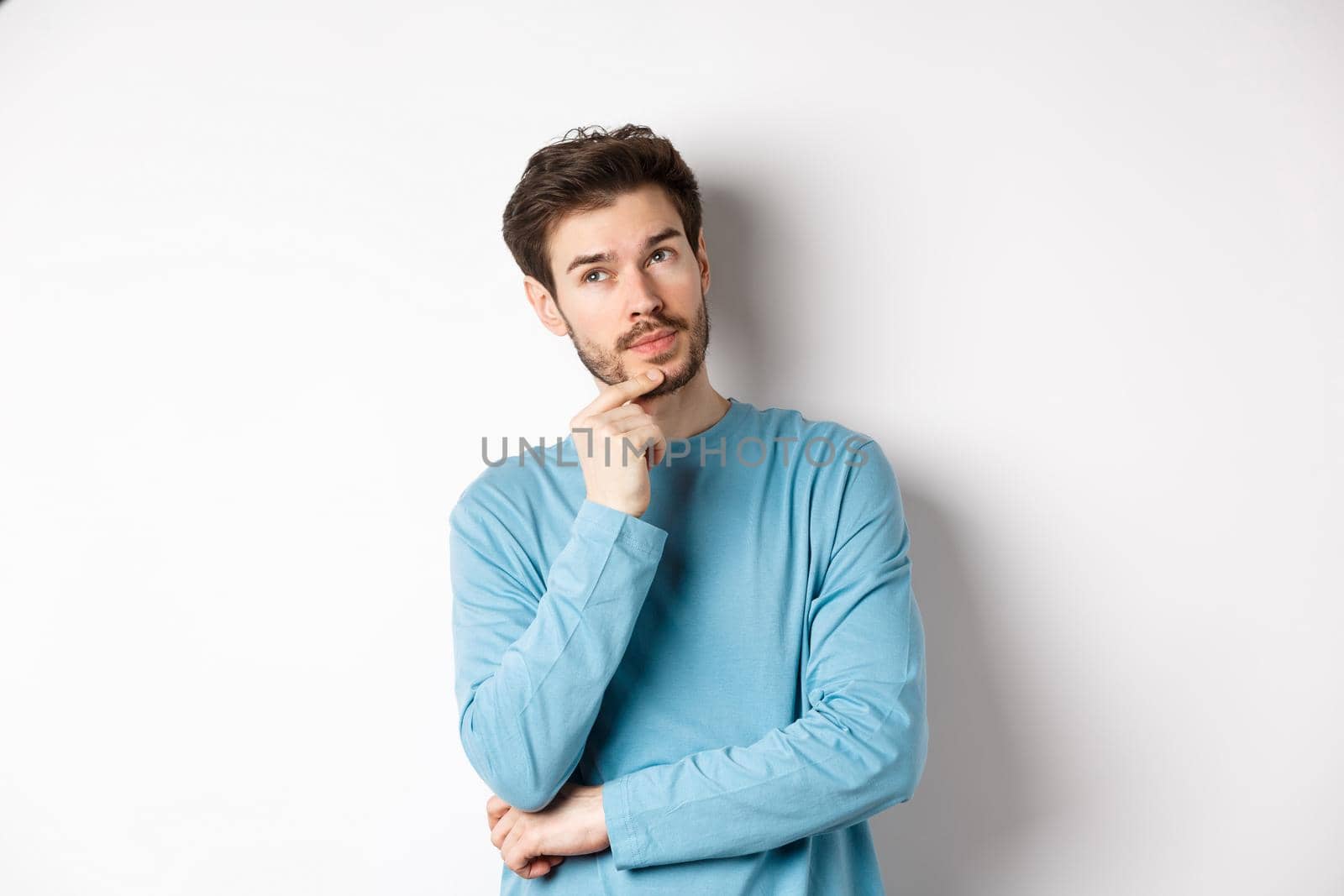Image of handsome young man making choice, thinking and looking pensive up, standing over white background.