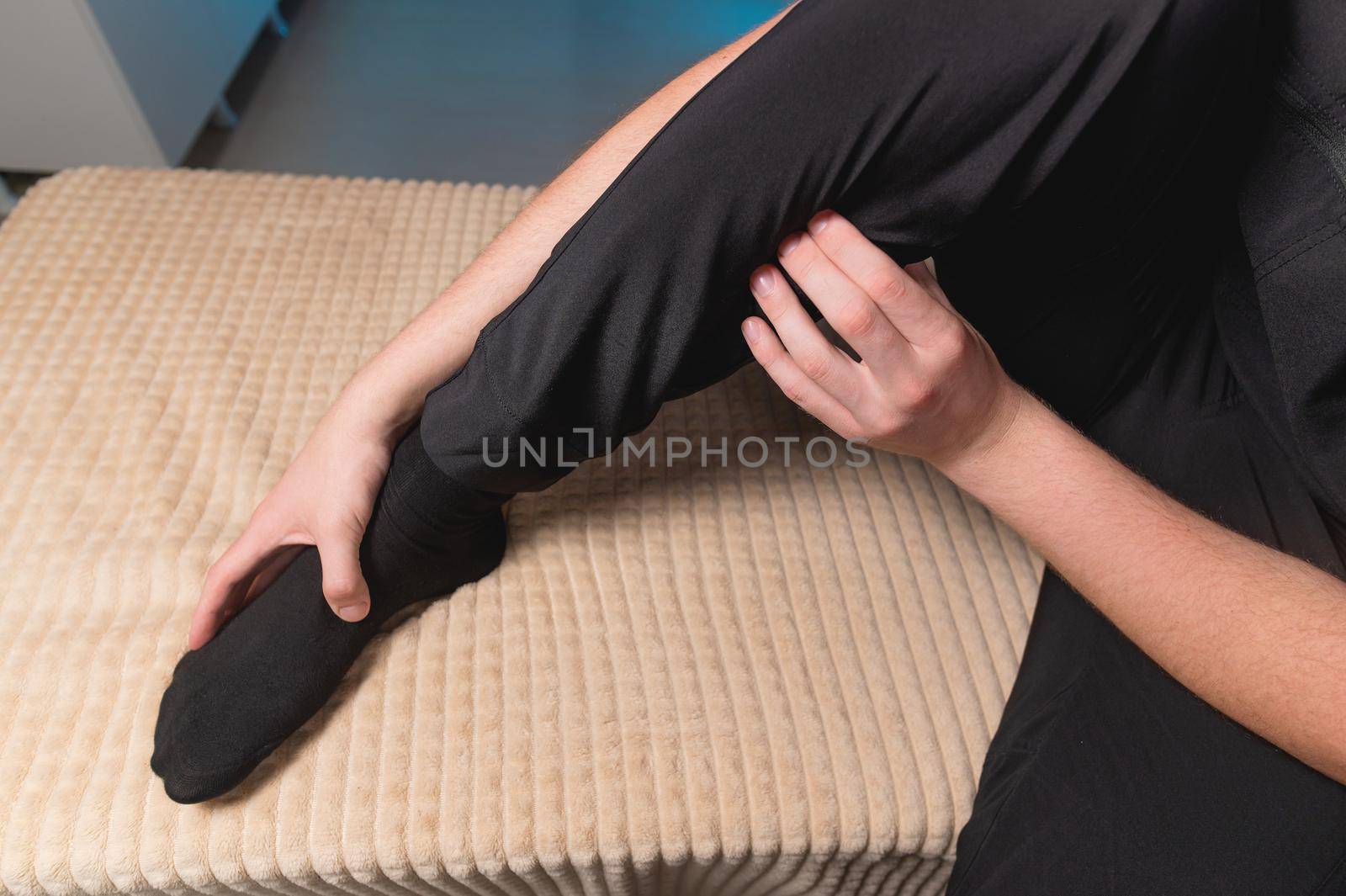 Caucasian male masseur doing self-massage for himself myofasceal release of the gastrocnemius muscle and ankle joint while sitting on the massage table. Self-administration of health improvement classes.