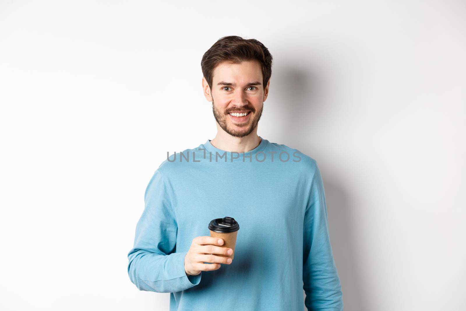 Cheerful man drinking coffee from cafe take-away and smiling, standing with paper cup in white background by Benzoix