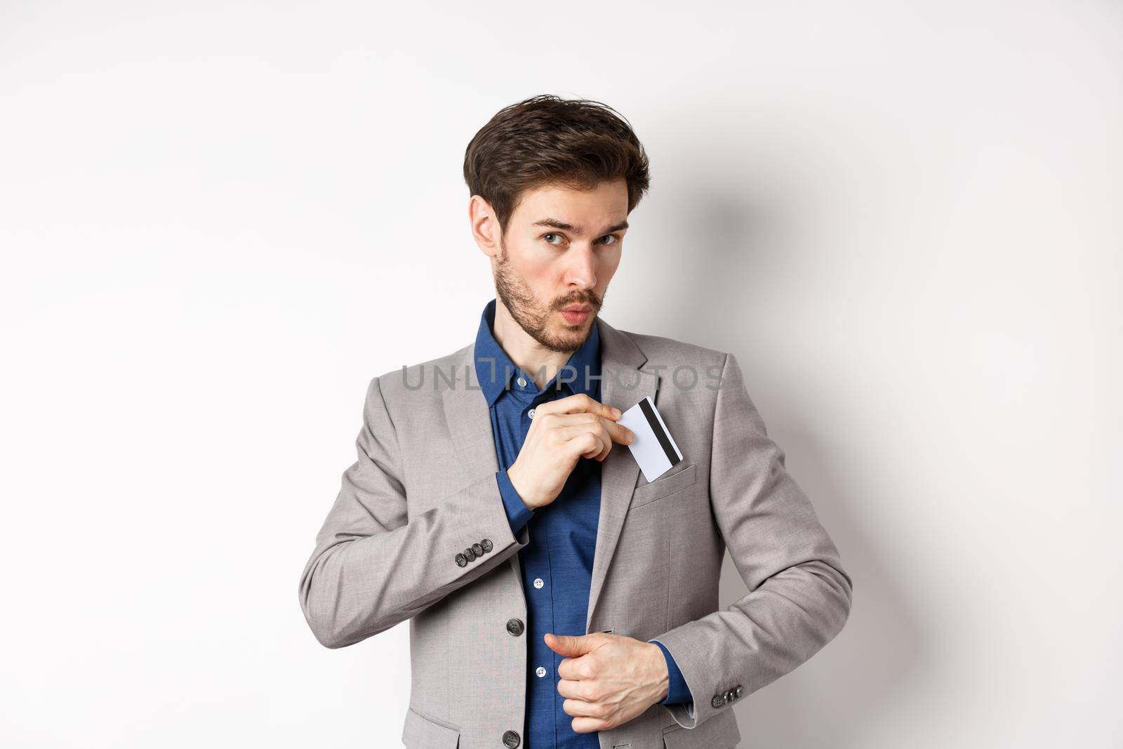 Businessman put credit card in suit pocket and whistling carefree, making shopping, standing on white background.