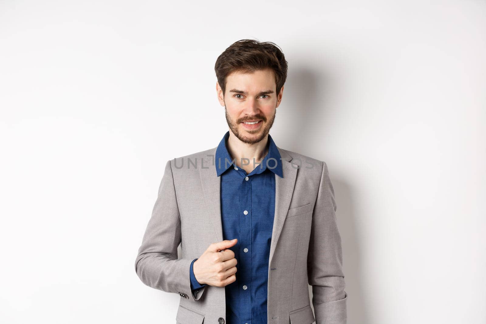 Confident businessman in suit smiling at camera, standing self-assured against white background by Benzoix