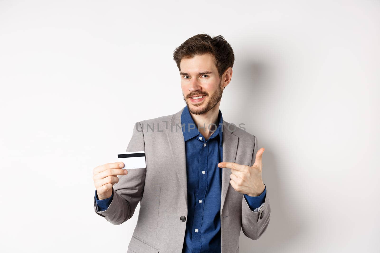 Successful male entrepreneur pointing at plastic credit card and smiling, recommending bank, standing on white background by Benzoix