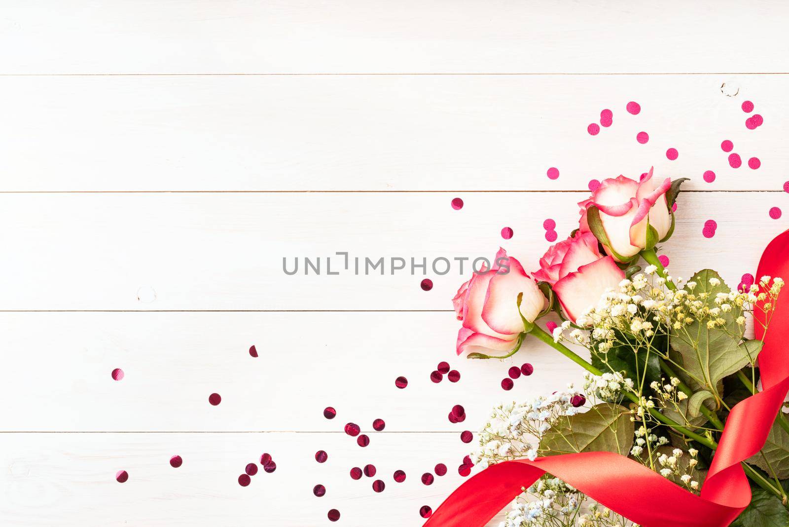 Valentines Day concept. Pink roses with confetti on white wooden background