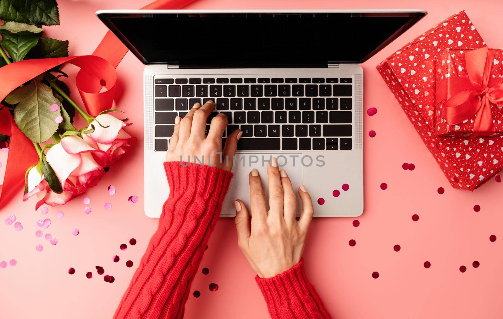 Valentines Day concept. Female hands typing on the keyboard, top view on pink background. Top view of pink desktop with flowers and gift boxes