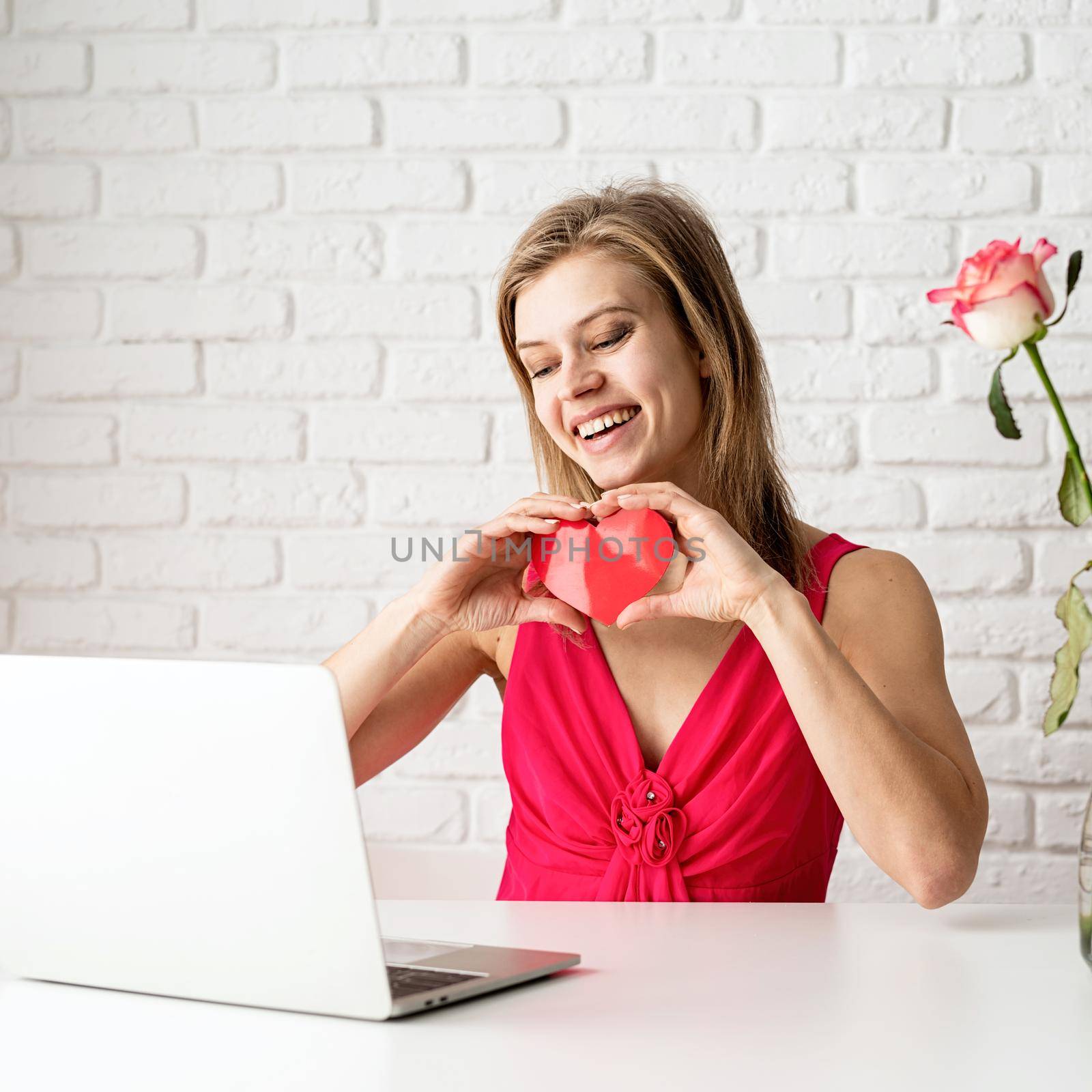 Valentines Day. Beautiful woman in pink dress dating online holding a heart in her hands