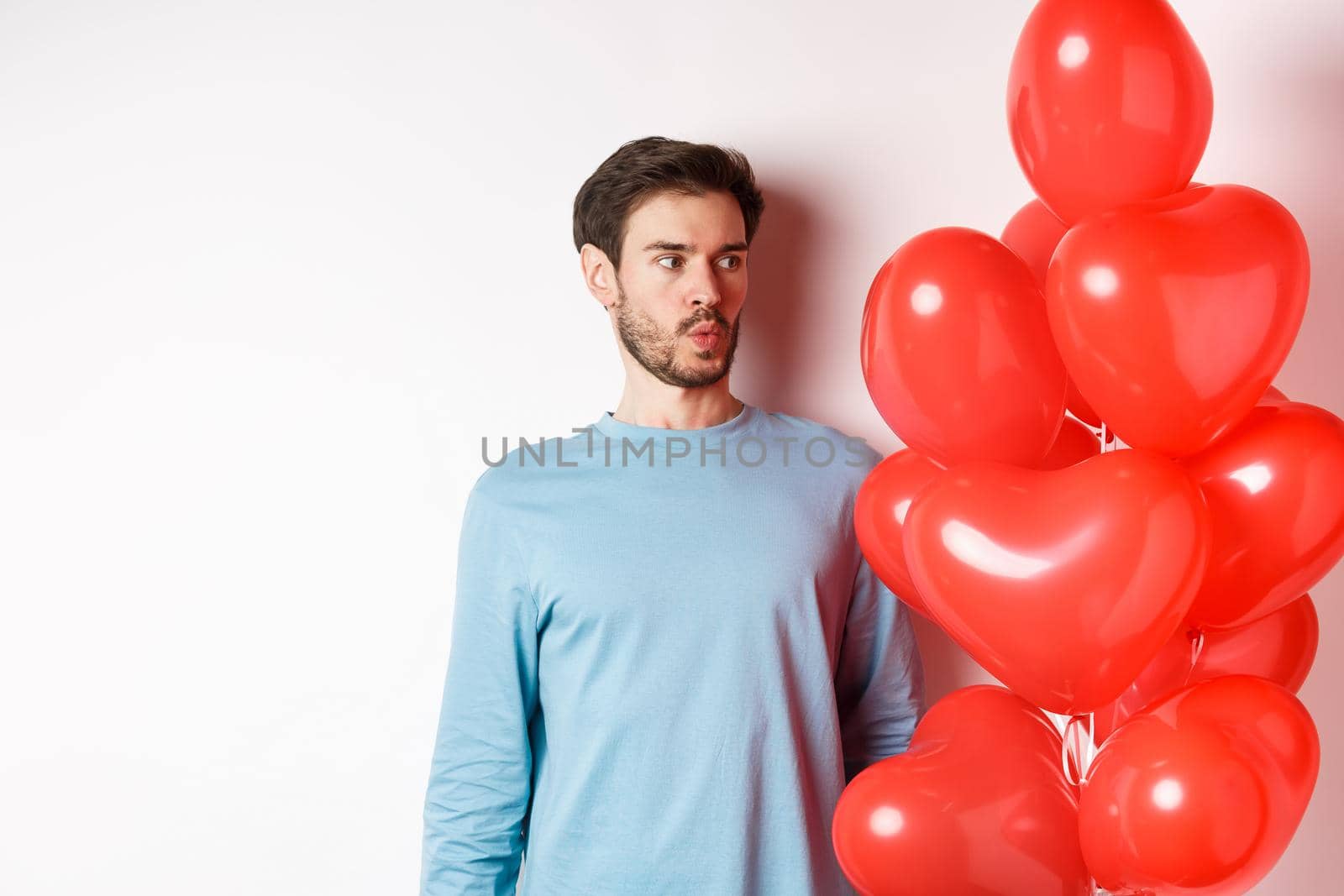 Relationship. Young man looking confused at heart balloon, puzzled on valetines day, standing over white background.