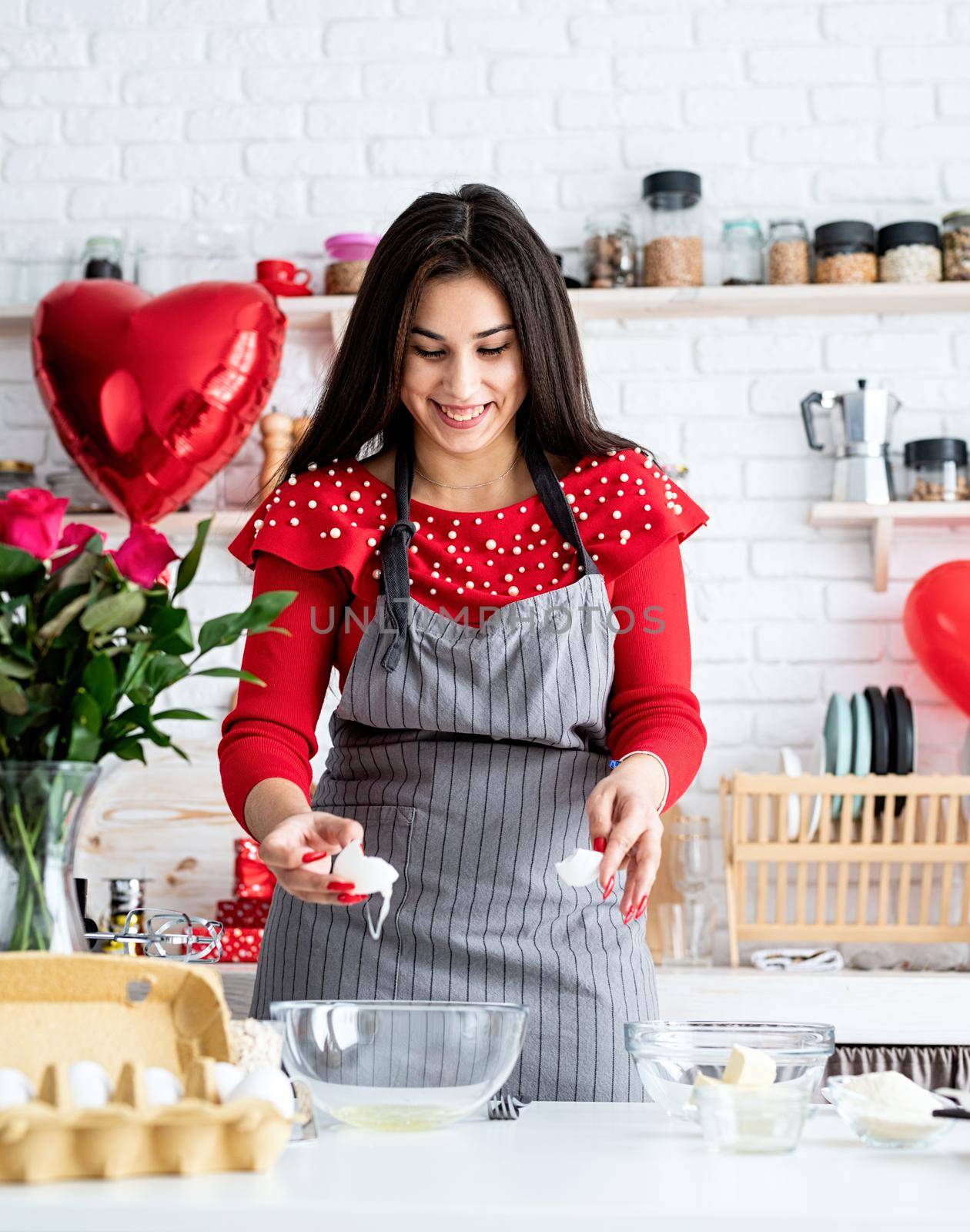Valentines Day. Woman in red dress and gray apron making valentine cookies at the kitchen