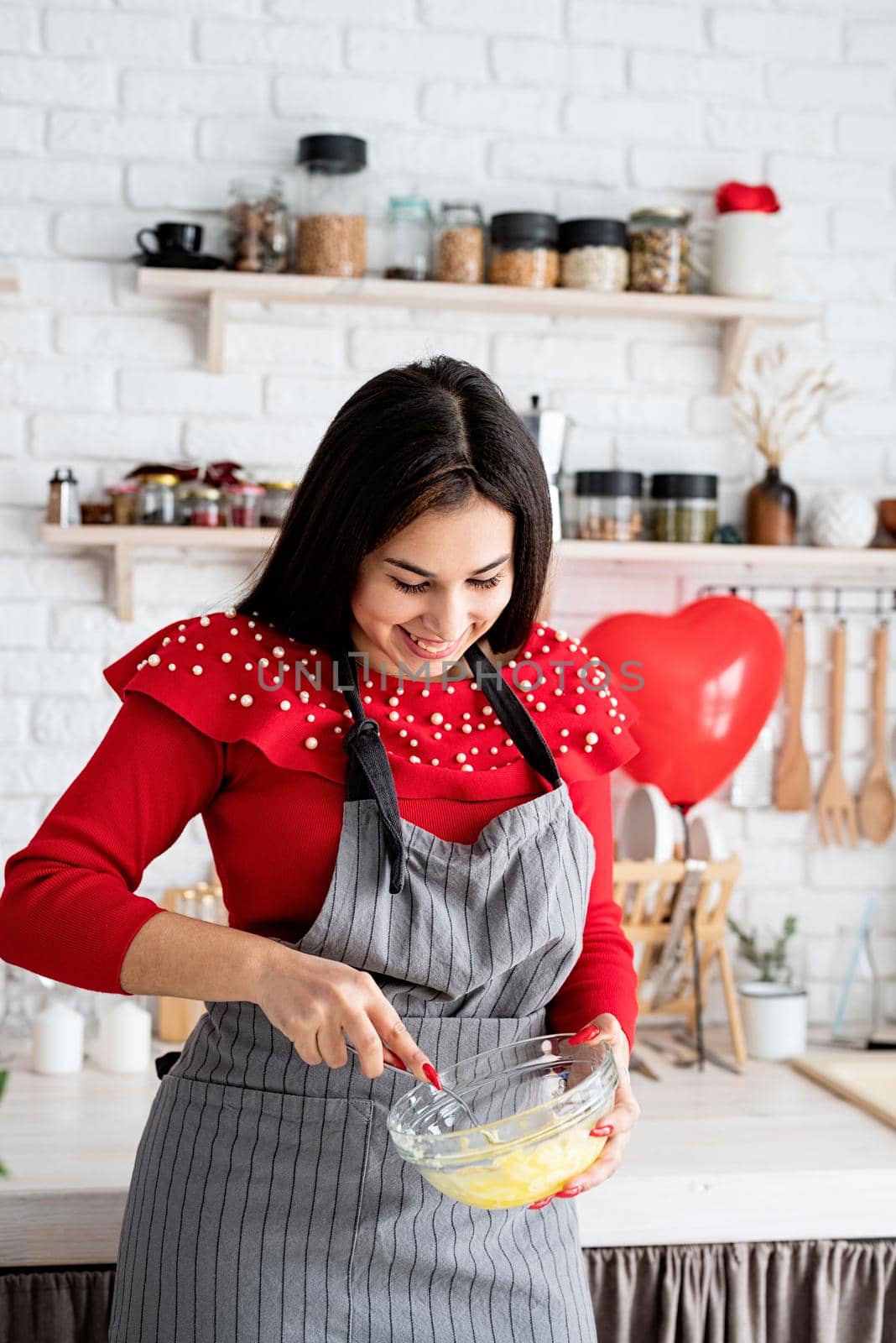 Woman in red dress and gray apron making valentine cookies at the kitchen by Desperada