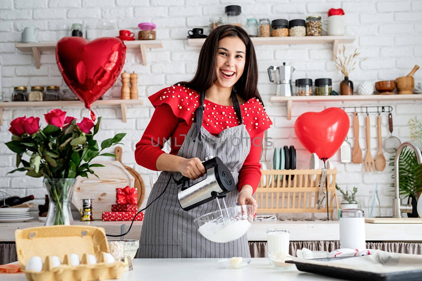 Woman in red dress and gray apron making valentine cookies at the kitchen by Desperada